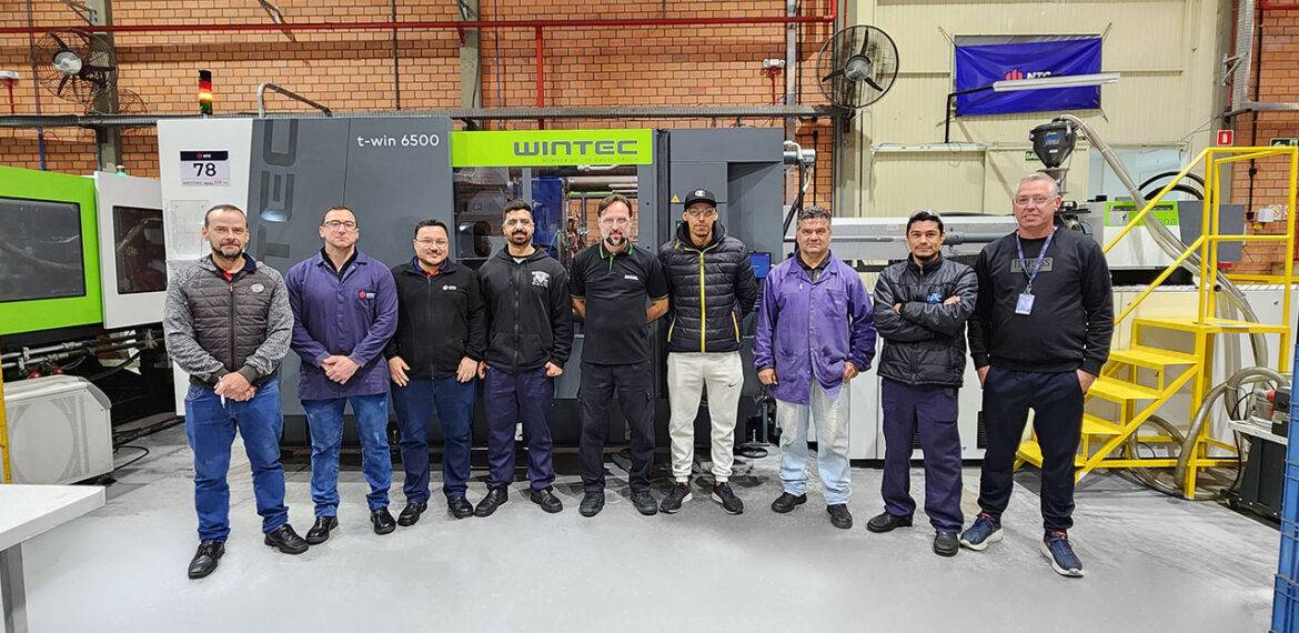 Equipe técnica da NTC e instrutor da ENGEL reunidos durante o treinamento, em frente a injetora WINTEC ENGEL t-win 6500.
