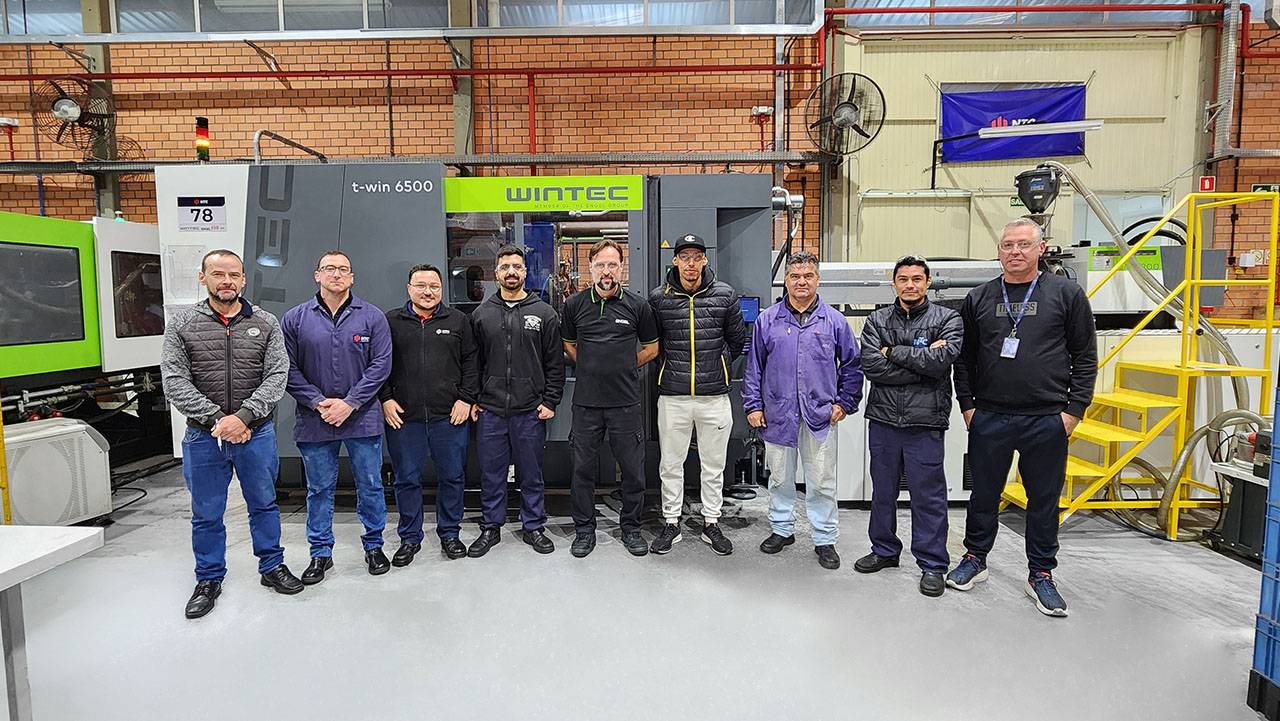 Equipe técnica da NTC e instrutor da ENGEL reunidos durante o treinamento, em frente a injetora WINTEC ENGEL t-win 6500.