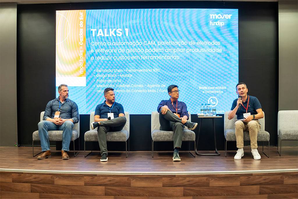Foto frontal dos quatro palestrantes no palco. O diretor Bernardo Shen, da NTC, aparece como o terceiro da esquerda para a direita, sentado e ouvindo a fala de um dos participantes. A tela ao fundo mostra o tema do painel.