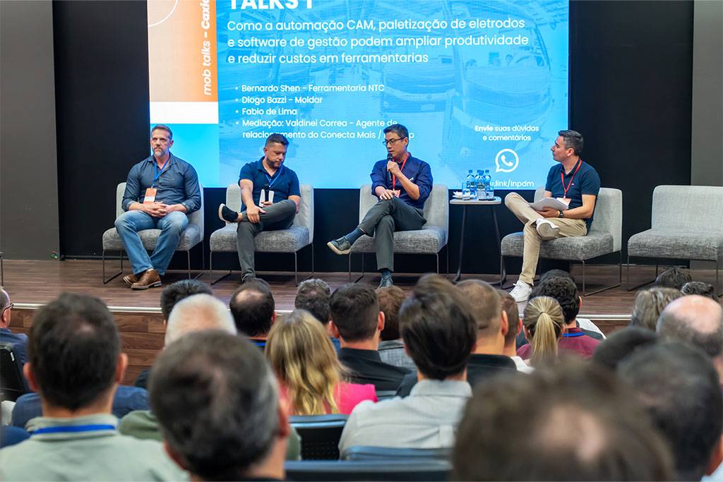 Plateia acompanhando o painel com quatro palestrantes no palco. O diretor Bernardo Shen, da NTC, está na terceira posição da esquerda para a direita, participando da discussão. A grande tela ao fundo exibe o conteúdo do evento.